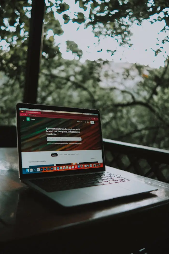 About Open laptop showing a website screen on a wooden table in an outdoor terrace setting.